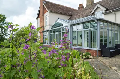 a conservatory with glass doors and purple flowers at Ashfield Place Farm by Group Retreats in Stowmarket