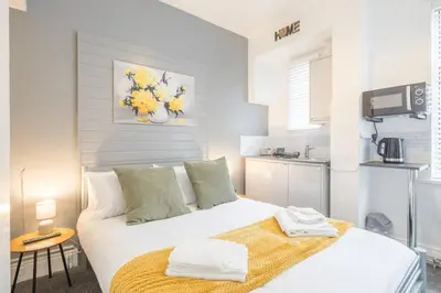 a white bedroom with a bed and a kitchen at The Modern Cambridge Studio 2 in Chesterton