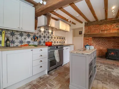 a kitchen with white cabinets and a brick wall at South Grange House - Sleep 16 in Saxmundham