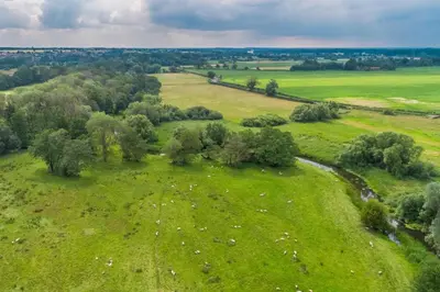 an aerial view of a green field with trees and a river at 1 Bed in Quidenham oc-2232 in Quidenham