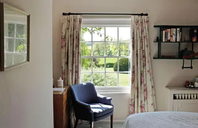 a bedroom with a blue chair and a window at The Old Rectory, Kettlebaston in Lavenham