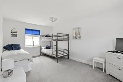 a white bedroom with a bunk bed and a television at Beach Front House in Walton-on-the-Naze
