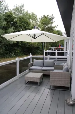 a patio with an umbrella and couches on a deck at Platinum lodge on Carlton Meres holiday Park in Rendham