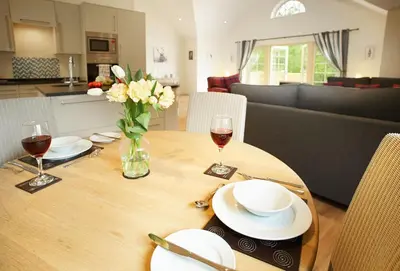 a wooden table with a vase of flowers and wine glasses at Brook Lodge Essex in Chappel