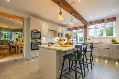 a kitchen with white cabinets and a island with bar stools at The Farmhouse, Nether Hall Estate in Pakenham