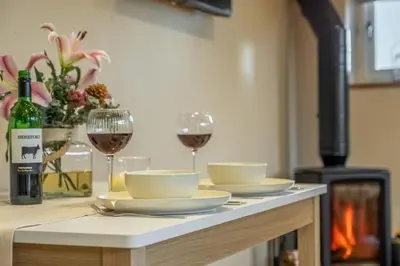 a table with two glasses of wine and a table with plates and bowls at Bumblebee Cottage in Barnham