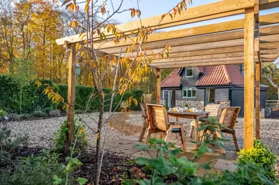 a wooden pergola with a table and chairs in a garden at Bumblebee Cottage in Barnham