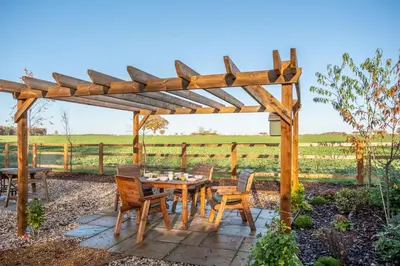 a wooden pergola with a table and chairs at Bumblebee Cottage in Barnham