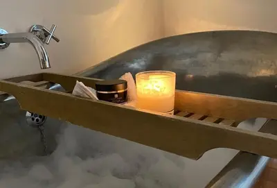a candle on a shelf in a bath tub with a sink at Blacksmith's Cottage Suffolk in Lavenham