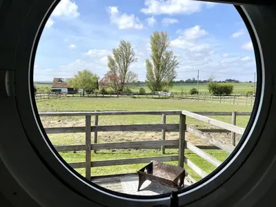 a round window looking out at a farm field at Armadilla 3 at Lee Wick Farm Cottages & Glamping in Clacton-on-Sea