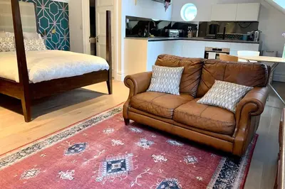 a living room with a brown couch and a bed at Scholar's Loft - Cosy & Close to Central Cambridge in Cambridge