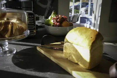 a loaf of bread on a cutting board with a bowl of fruit at Moulton Lawn House B&B in Moulton