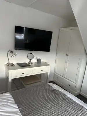 a bedroom with a white desk with a television on the wall at Isabella Rooms in Hockley