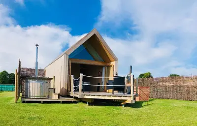 a small house with a porch on a grass field at Lushna 1 Mezzanine at Lee Wick Farm Cottages & Glamping in Clacton-on-Sea