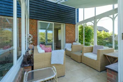 a screened in porch with wicker chairs and tables at 9 The Coastguards in Thorpeness