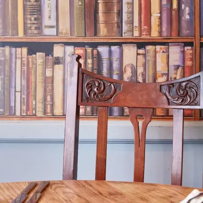 a wooden chair sitting in front of a book shelf at Swan Hotel by Greene King Inns in Thaxted