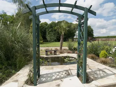 a green archway in a garden with a pond at St Andrews Barn in Necton