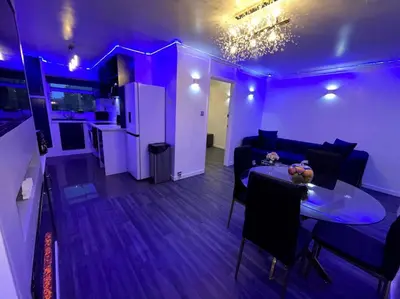 a living room with a table and a kitchen with purple lighting at Chic 2 Bedroom Flat in Trimley Heath
