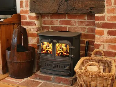 a wood stove in a brick fireplace with a basket at Valley Farm Cottage in Sudbourne