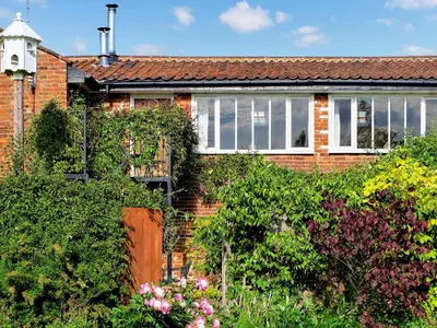 a red brick house with bushes and flowers at Dove Cottage in Halesworth