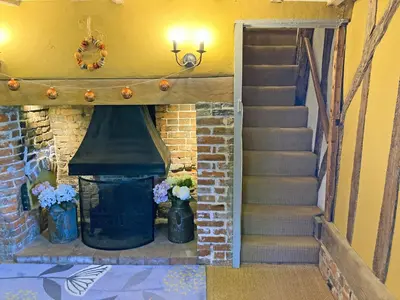 a staircase leading to a fireplace with flowers in vases at Bell Corner Cottage in Cratfield