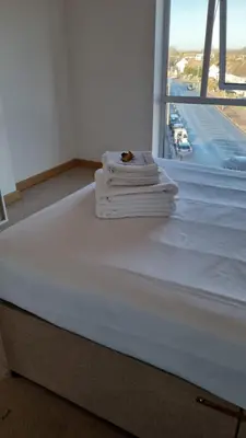 a stack of towels on a bed in a room with a window at Modern 2 bed flat with balcony in Southend-on-Sea