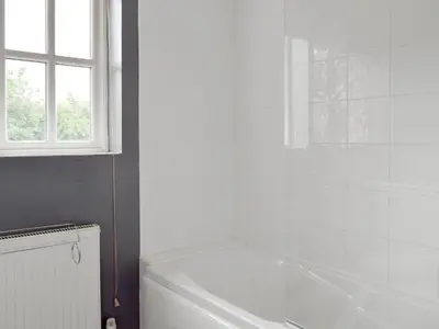 a white bathroom with a tub and a window at Dormers in Leiston