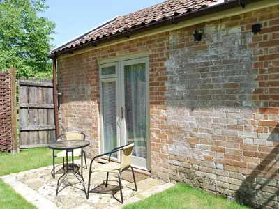 a patio with a table and chairs in front of a brick building at The Coach House in Saxmundham