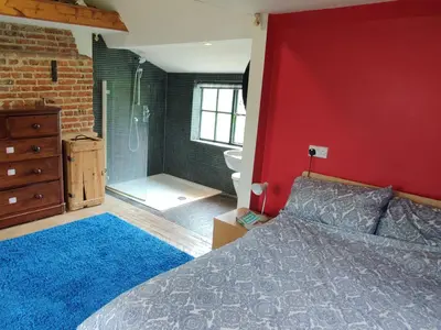 a bedroom with a bed and a red wall at Burnt House Cottage in Barking