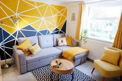 a living room with a blue couch and a geometric wall at Modern 2-Bed Duplex - 10 Mins to City Centre in Chesterton