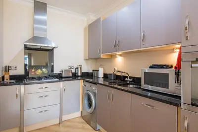 a kitchen with white cabinets and a washer and dryer at Camstay Longworth Avenue in Cambridge