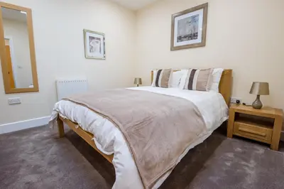 a white bedroom with a large bed and a mirror at Camstay Longworth Avenue in Cambridge