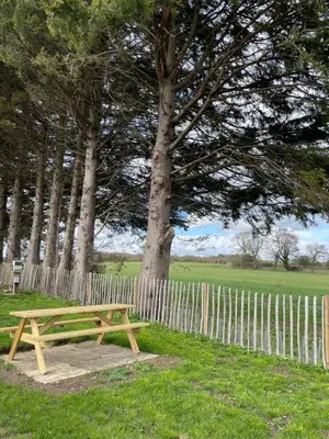 a wooden picnic table in a field next to a fence at Henny Riverside Glamping in Sudbury