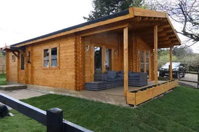 a small log cabin with a porch on the grass at Bishy Barnabees country lodge with hot tub in Swaffham