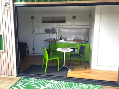 a kitchen with a table and green chairs in a room at Green CargoPod at Lee Wick Farm Cottages & Glamping in Clacton-on-Sea
