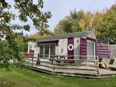a small cabin with a deck in the grass at Purple CargoPod at Lee Wick Farm Cottages & Glamping in Clacton-on-Sea