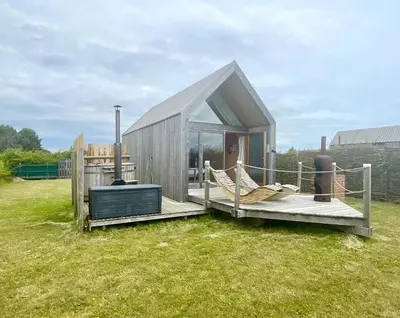 a small wooden house with a deck and a chair at Lushna 11 Lux Suite at Lee Wick Farm Cottages & Glamping in Clacton-on-Sea