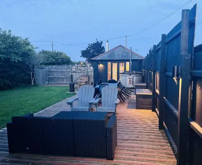 a deck with white chairs and a house at Stable Cottage at Lee Wick Farm Cottages & Glamping in Clacton-on-Sea