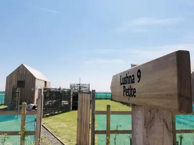 a wooden sign on a fence with a barn at Lushna 5 Petite at Lee Wick Farm Cottages & Glamping in Clacton-on-Sea