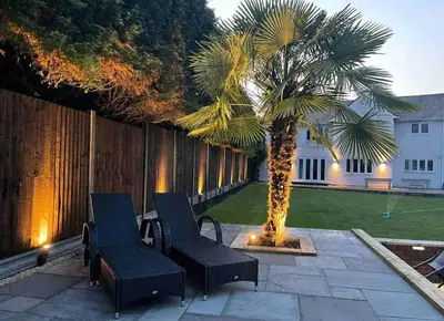 a patio with two chairs and a palm tree at Large Countryside House Swim Pool Jacuzzi Sleeps 10 guest in Ware