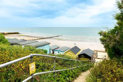 a beach with a row of beach huts and the ocean at Shore House - Walton in Walton-on-the-Naze