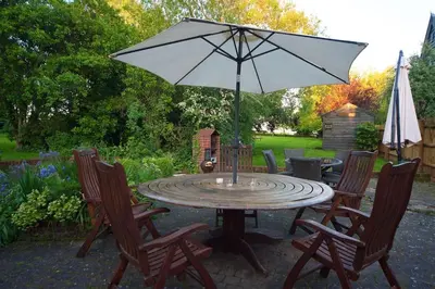 a patio table with an umbrella and chairs at Stunning barn conversion ideal for large families in Bildeston