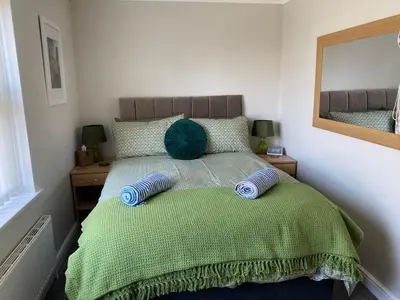 a bedroom with a bed with a green comforter and a mirror at La de da Frinton on Sea in Frinton-on-Sea