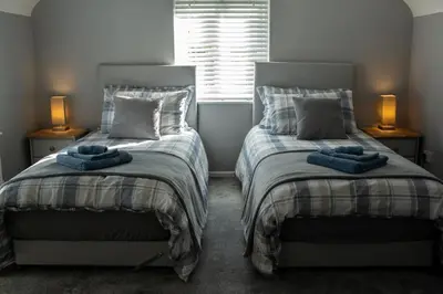two beds in a bedroom with two lamps and a window at Baytree Cottage Framlingham in Framlingham