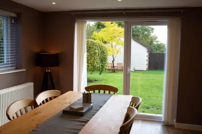 a dining room with a wooden table and a large window at Baytree Cottage Framlingham in Framlingham