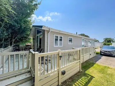 a house with a white fence and a car at Stunning Lodge With Decking At Oaklands Holiday Park In Essex Ref 39017Rw in Clacton-on-Sea