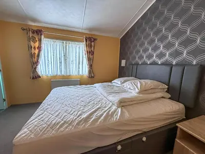 a large bed in a bedroom with a window at Stunning Lodge With Decking At Oaklands Holiday Park In Essex Ref 39017Rw in Clacton-on-Sea