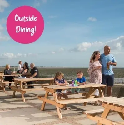 a group of people sitting at picnic tables at the beach at Happy Place in West Mersea