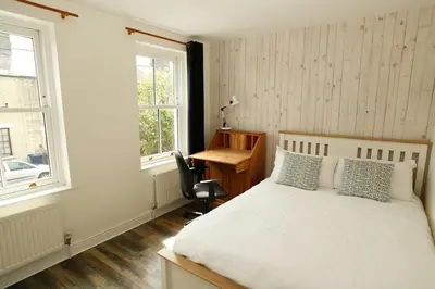 a bedroom with a bed and a desk and two windows at Vibrant Mill Road Oasis - Peaceful House with Garden near station in Cambridge