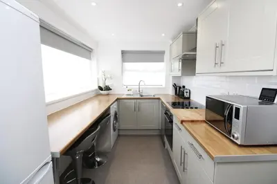a kitchen with white cabinets and a wooden counter top at Modern and Cosy Flat For 4 in Cherry Hinton